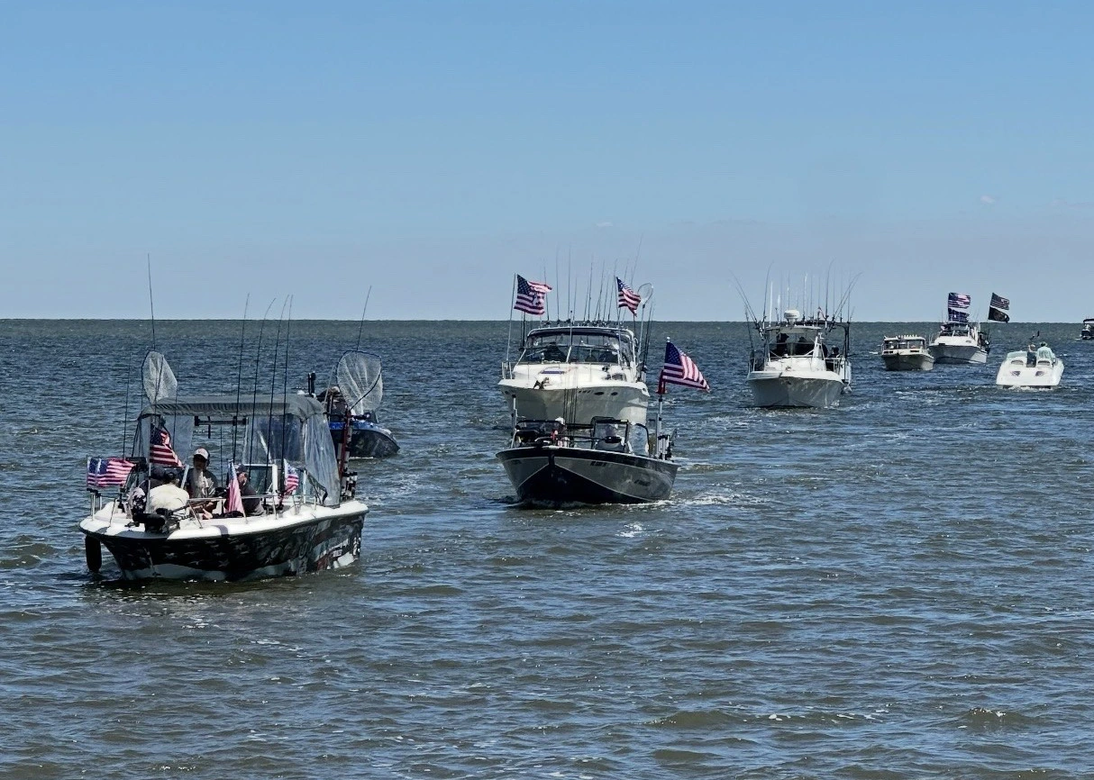 Line of boats out on the water in Bay City with flags and local veterans.