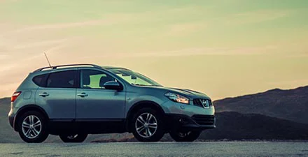 Silver SUV parked on a scenic overlook at sunset with mountains in the background.
