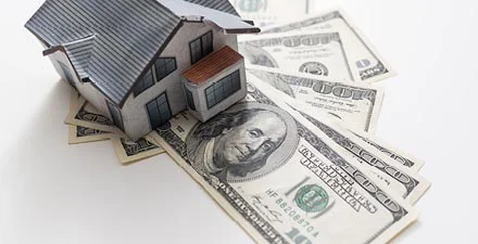 Model house placed on top of several hundred-dollar bills.