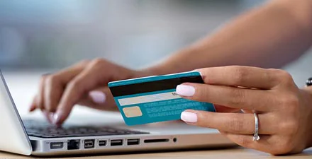 Hand holding a credit card while typing on a laptop keyboard for an online payment.