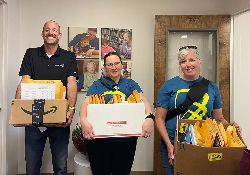 Three Wildfire employees smiling and delivering books to Saginaw READ association.
