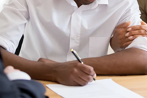 Man in white shirt signing a document with a pen.