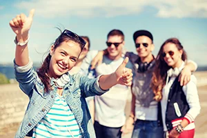 Group of five happy young adults posing outdoors with one giving thumbs up.