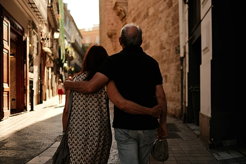 Couple walking downtown street in historic city arm in arm in the shade.