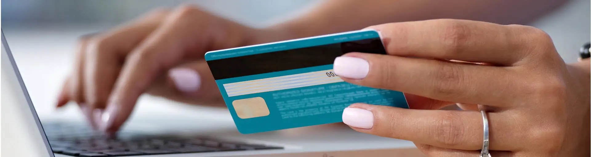 Hands holding a teal debit or credit card and typing on a laptop.