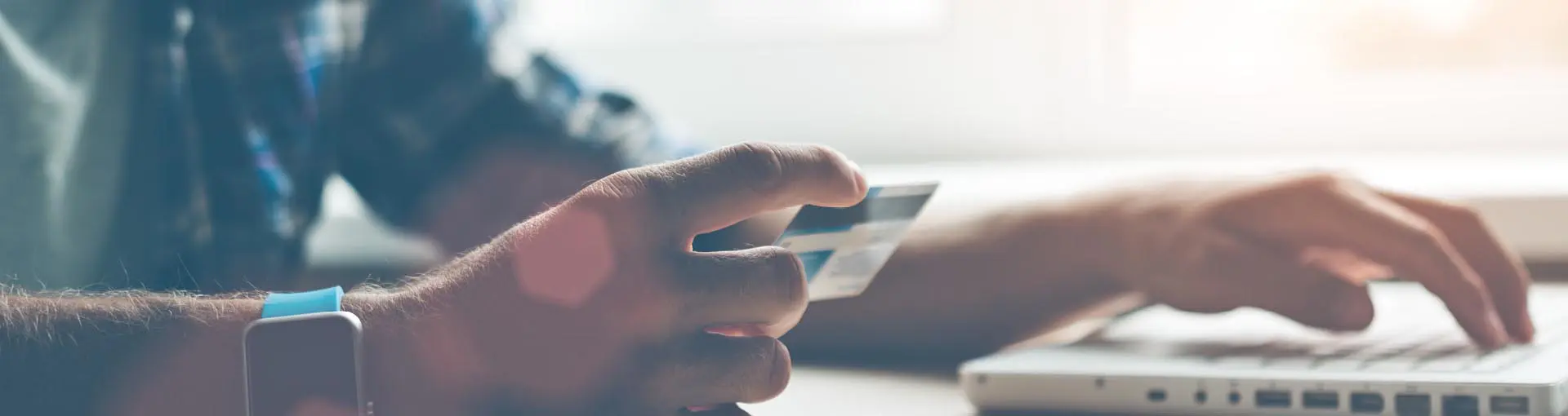 A man in blue flannel with smart watch typing a debit card number into a laptop.