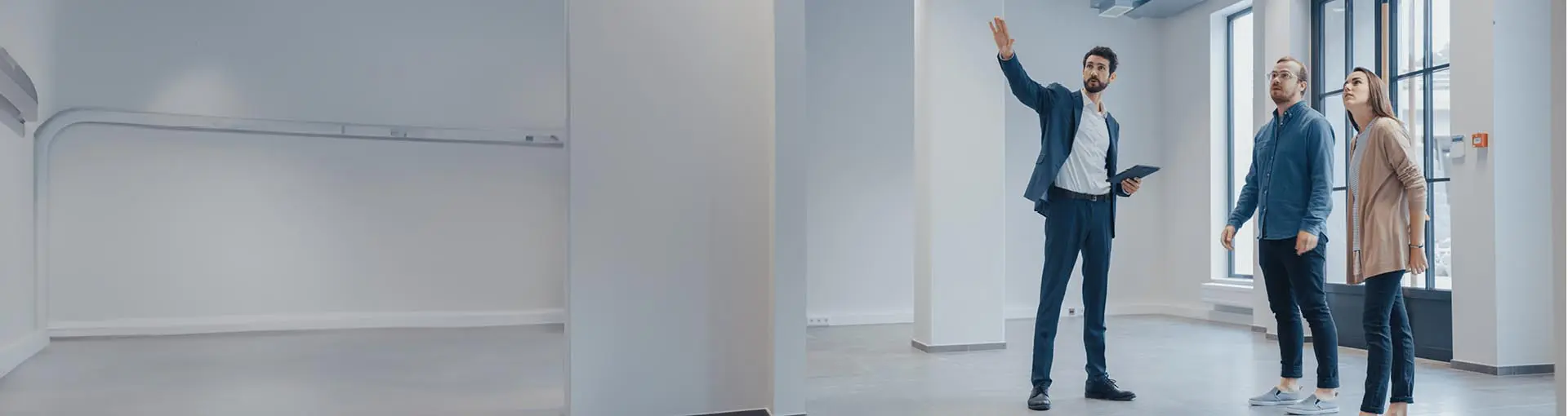 Real estate agent showing a modern, empty commercial space to a couple near large windows.