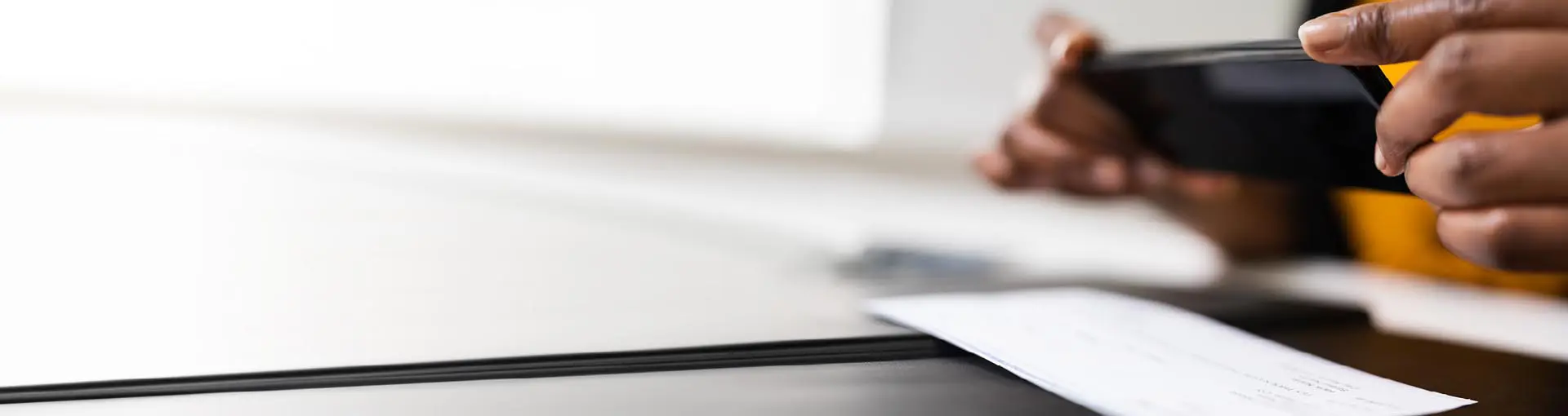 Person using a smartphone to deposit a check on a desk with a blurred background.