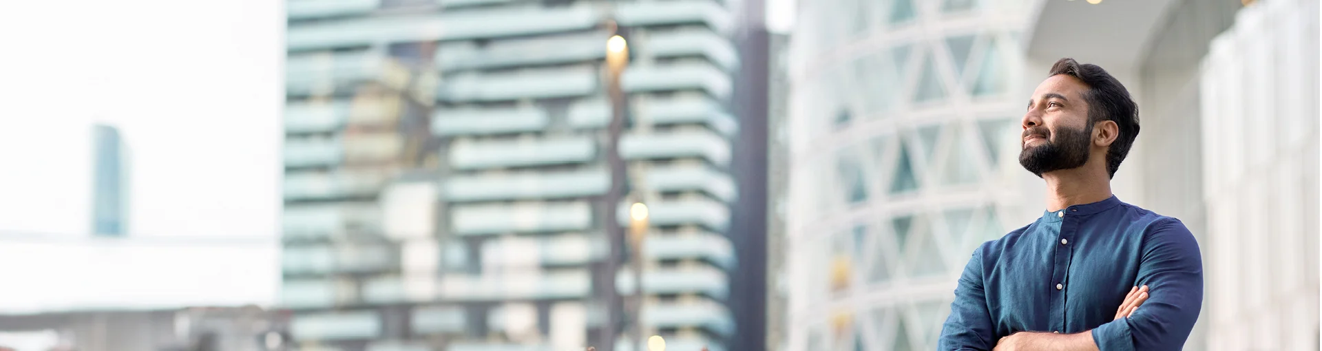 Man in blue shirt looking up in bright downtown city with skyscrapers.