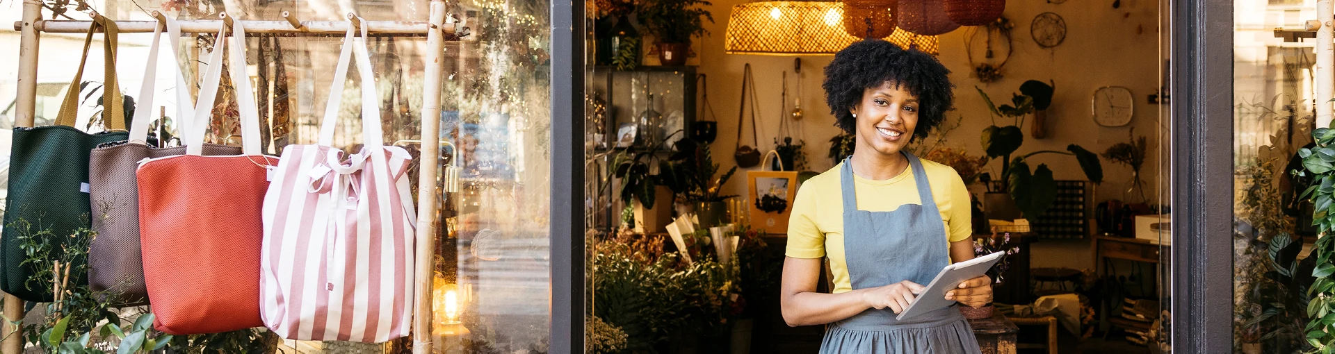 Female business owner standing in front of her boutique store with various bags and products for sale .