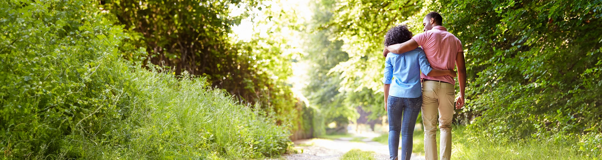 Happy couple walking arm and arm together down a two track trail in woods.