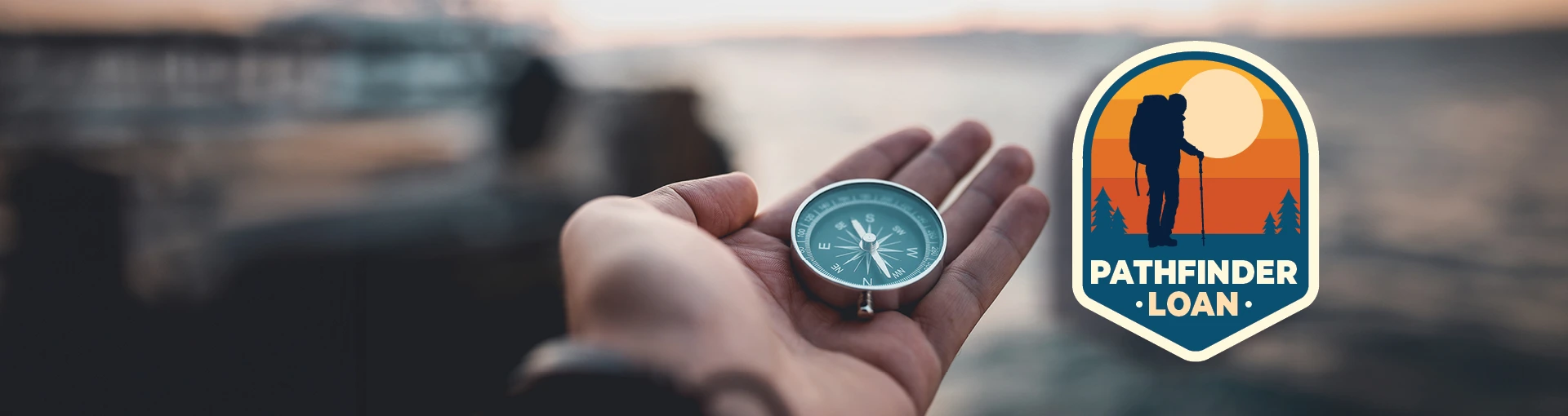Person holding a compass overlooking the water with a Pathfinder Loan badge next to it.