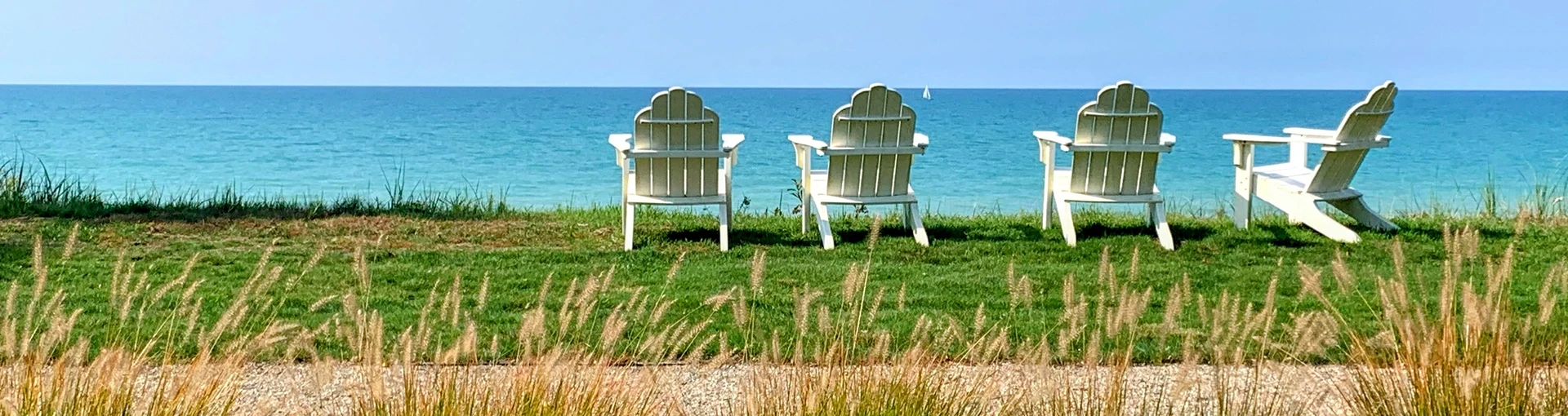 Four white charis on grass overlooking the clear blue water of Lake Michigan.