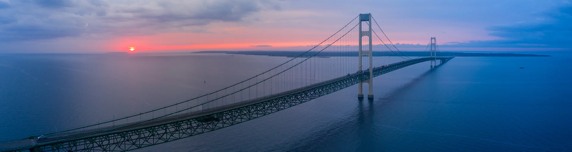 Aerial view of Mackinac Bridge at cloudy red sunset in the distance and slightly foggy.