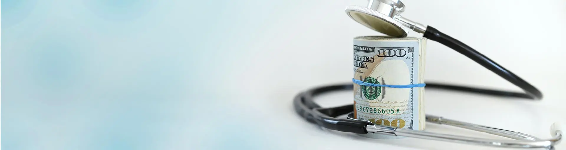 Stethoscope wrapped around a roll of $100 bills on a light blue background.