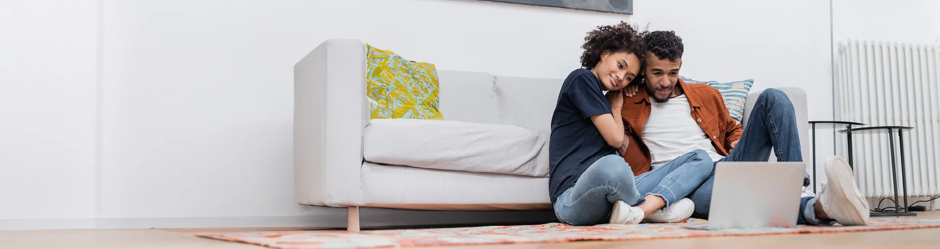 Couple sitting on living room floor in front of couch looking at laptop.