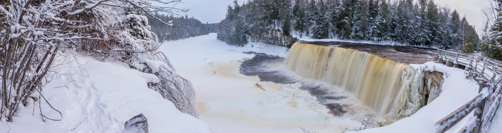 Winter view of Tahquamenon Falls State Park with water rushing over.