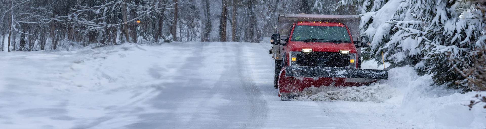 Red business truck plowing snow down a driveway.