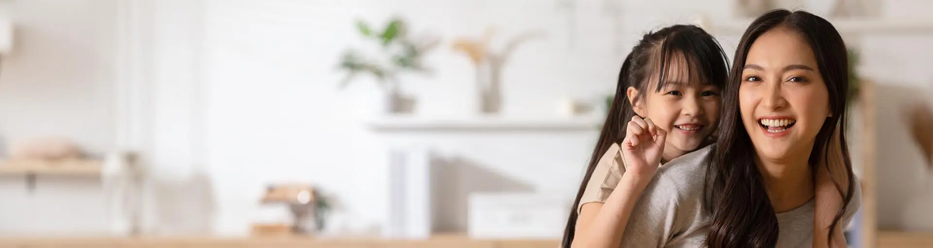 Mother giving daughter a piggy back ride in modern white kitchen.