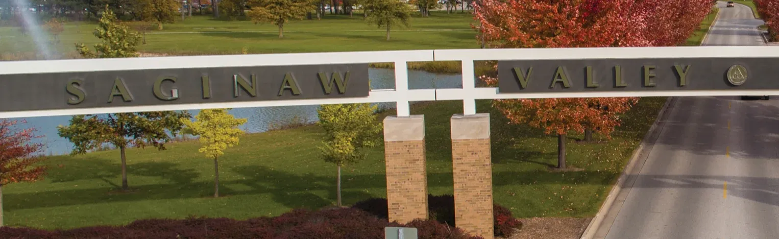 Entrance archway to Saginaw Valley State University with fall trees and campus buildings in the background.