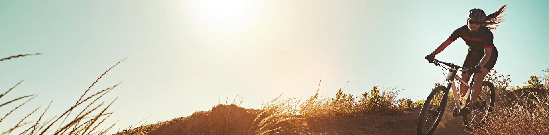Woman riding mountain bike down a sandy hill during sunset.
