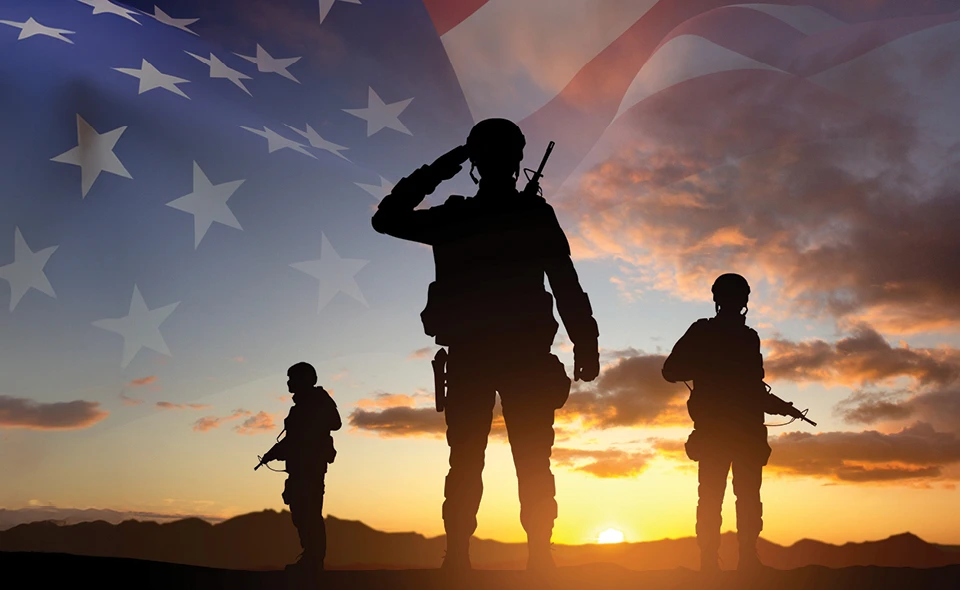 Group of three soldiers standing with a sunset and american flag on the horizon.